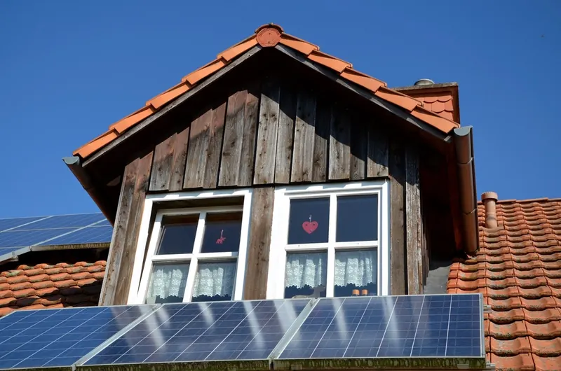 Lucarne en bois au-dessus de panneaux solaires sur un toit en tuiles